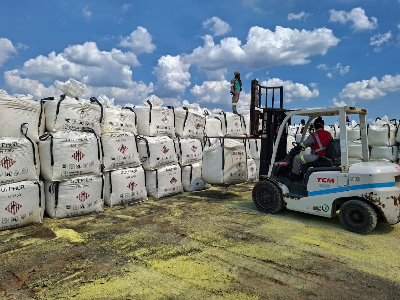Labeled Sulphur UN 1350 jumbo bags being loaded by forklift under a clear blue sky
